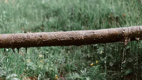 Rusted Metal Leaking Pipe above Grassy Meadow